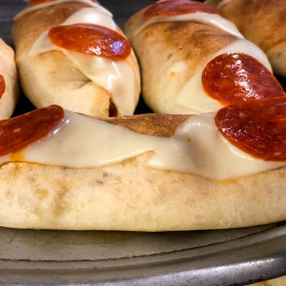Close-up of baked pepperoni pizza boats with melted cheese arranged on a metal baking tray.
